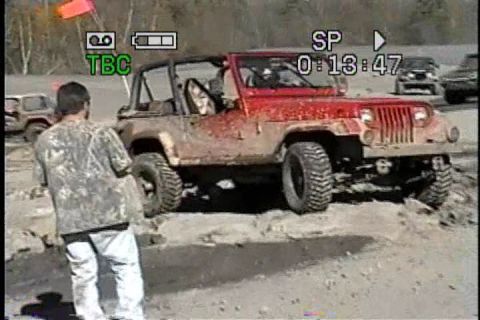 1989 Ford Bronco - A man observes a red Jeep Wrangler covered in mud during an off-road excursion.