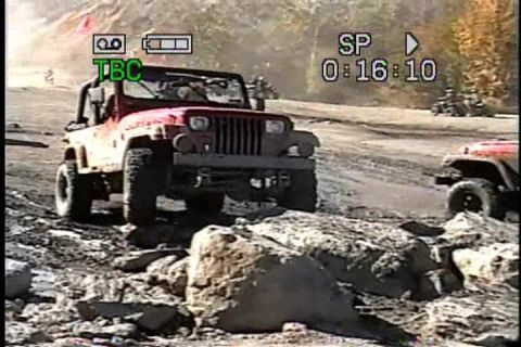 1989 Ford Bronco - A red Jeep Wrangler navigates a rocky off-road course, with another Jeep visible in the background.