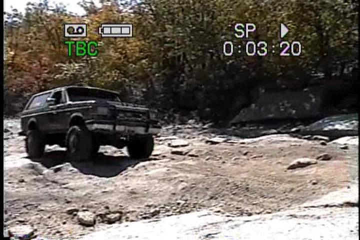 1989 Ford Bronco driving on a rocky trail with trees in the background