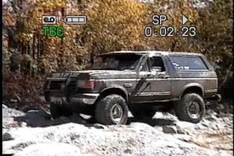 1989 Ford Bronco - A 1987 Ford Bronco navigates a rough, off-road path with trees in the background.