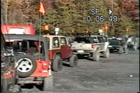 1989 Ford Bronco - Multiple off-road vehicles are parked in a line on a dirt surface, with trees visible behind them.
