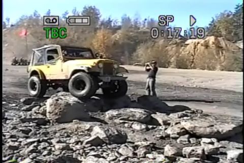 1989 Ford Bronco - A yellow off-road vehicle tackles a challenging rocky course, with a person observing in the background.
