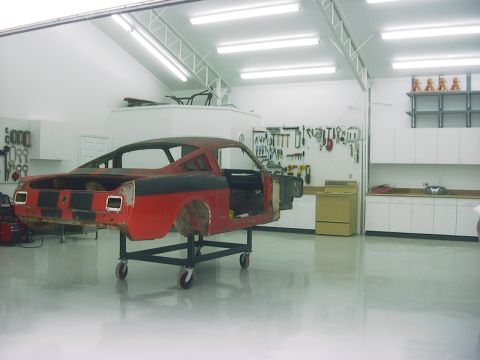 1990 Ford Mustang - Car body on a rolling stand in a well-lit garage, undergoing restoration.