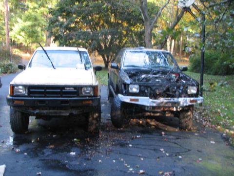 1994 Toyota Tacoma - Two Toyota trucks are parked side-by-side, with the black truck's hood open, revealing its engine.
