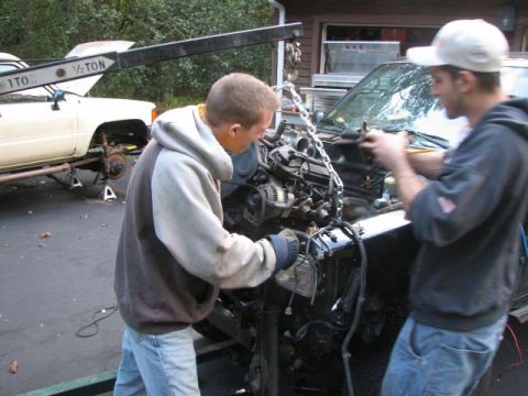 1994 Toyota Tacoma - Two men work on removing an engine from a truck, with another truck visible in the background.