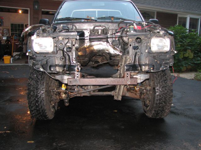 Truck front end with fenders and hood removed, showing engine bay and suspension components
