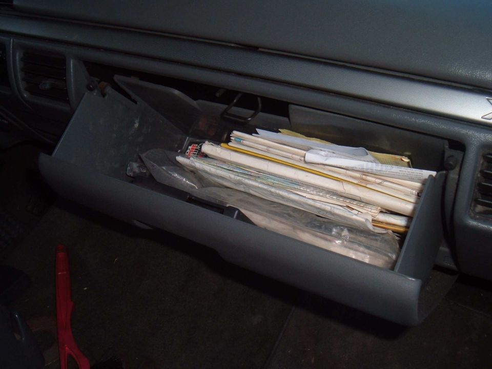 Open gray glove compartment filled with papers and plastic-wrapped items