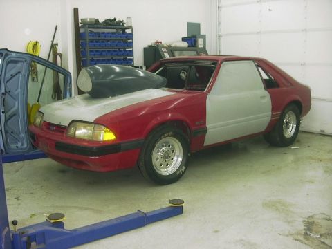 1990 Ford Mustang - This 1990 Ford Mustang is in a garage, possibly undergoing modifications, with a large hood scoop visible.