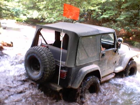 2001 Ford Escape - This Jeep Wrangler is navigating a water obstacle, kicking up mud and spray.