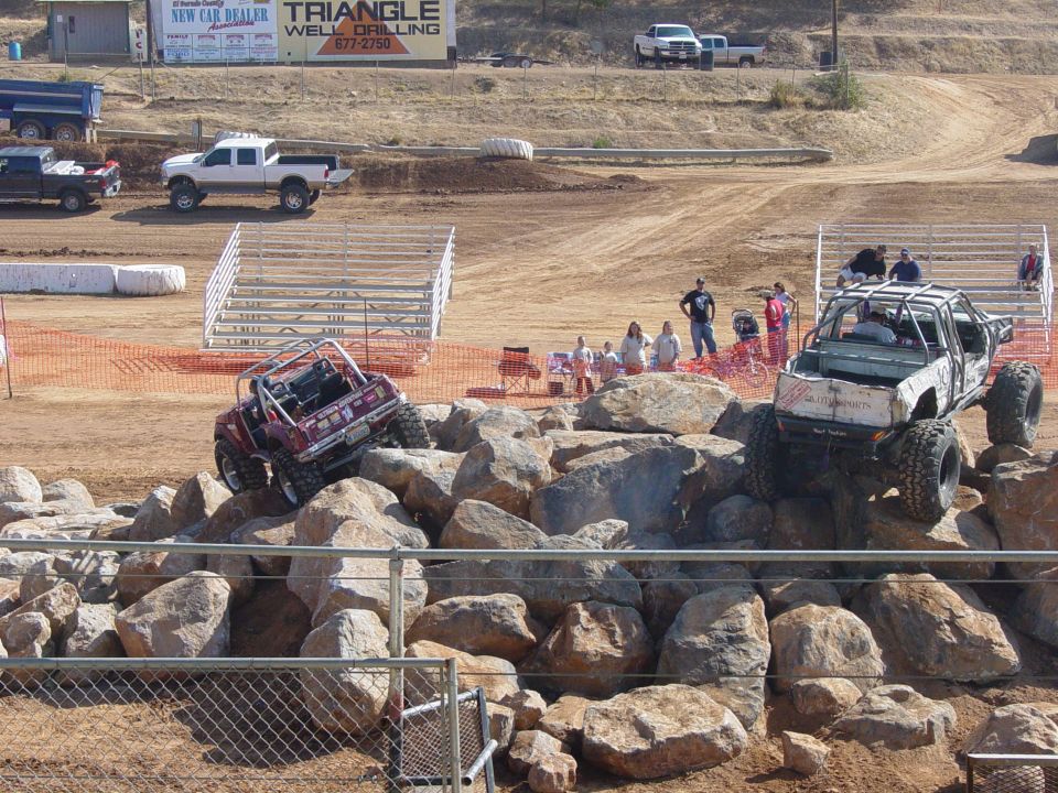 Two modified off-road vehicles climbing over large rocks at an event