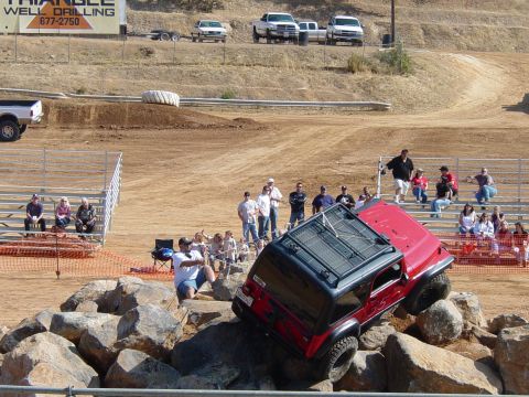 1986 Ford Bronco - A red Jeep Wrangler is shown attempting to traverse a challenging rock obstacle during an event.