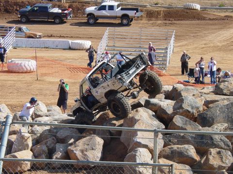1986 Ford Bronco - A modified off-road vehicle navigates a rocky obstacle course, with spectators watching from the sidelines.