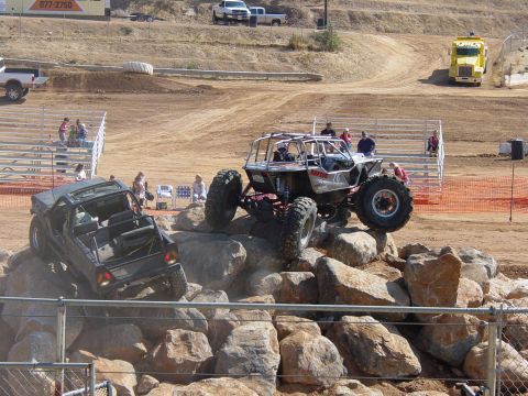 1986 Ford Bronco - Two highly modified off-road vehicles tackle a challenging rock crawling course with spectators watching from the sidelines.