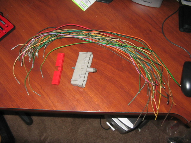 Bundle of multicolored wires with crimped ends, a gray electrical connector, and a red connector piece on a wooden desk