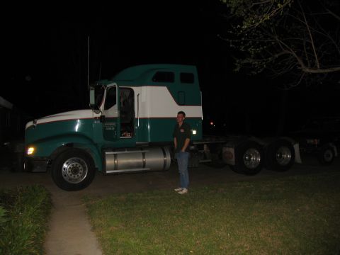 1988 Ford C-350 (Centurion Conversions) - Man stands next to a green and white semi-truck tractor parked on a grassy area at night.