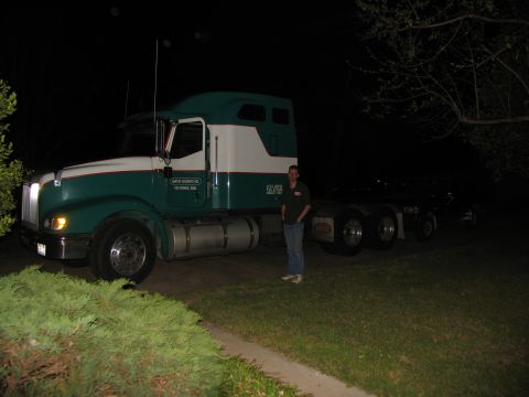1988 Ford C-350 (Centurion Conversions) - A person stands next to a semi-truck tractor at night, with some text visible on the side of the cab.