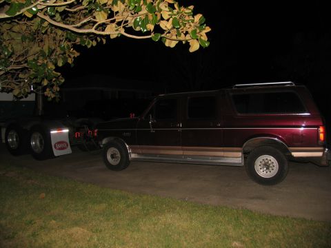 1988 Ford C-350 (Centurion Conversions) - A custom extended Ford Bronco SUV is towed by a semi-truck at night.