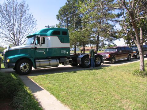 1988 Ford C-350 (Centurion Conversions) - A semi-truck is seen towing a maroon SUV, with a person standing between them.