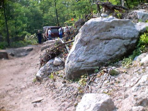 2001 Ford Escape - Several people stand around two vehicles on a rough, wooded trail with large boulders.