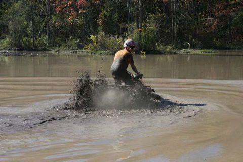 1987 Ford Bronco - An ATV rider creates a large splash as they navigate through a muddy body of water on a sunny day.