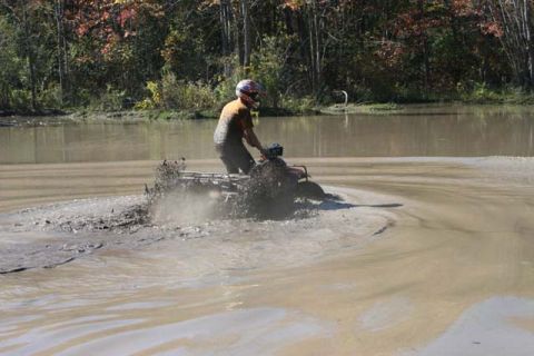 1987 Ford Bronco - A person rides a quad bike through muddy water, kicking up a large spray.
