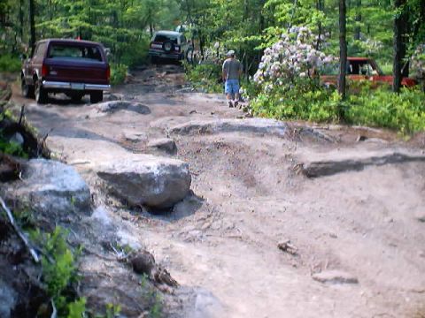 2001 Ford Escape - Multiple off-road vehicles navigate a challenging rocky trail through a wooded area.