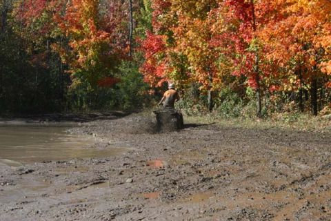 1987 Ford Bronco - An ATV kicks up mud on a trail surrounded by colorful autumn trees.