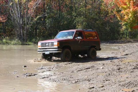 1987 Ford Bronco - A red Ford Bronco II navigates a muddy trail during autumn.