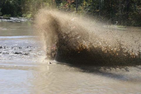 1987 Ford Bronco - An off-road vehicle creates a large splash as it drives through a muddy area.