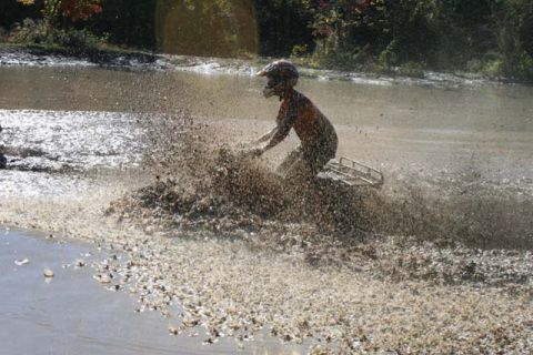 1987 Ford Bronco - An ATV rider navigates through a muddy puddle, sending water and dirt flying.