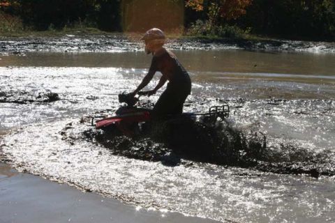 1987 Ford Bronco - ATV rider navigates a muddy trail, kicking up water and dirt.