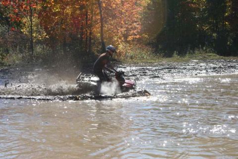 1987 Ford Bronco - ATV rider navigates a muddy trail during autumn with colorful foliage overhead.