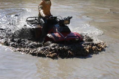 1987 Ford Bronco - An ATV navigates through a muddy terrain, kicking up water and dirt.