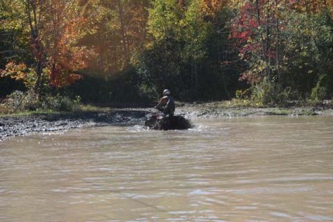1987 Ford Bronco - ATV rider navigates through a muddy water crossing surrounded by autumn foliage.