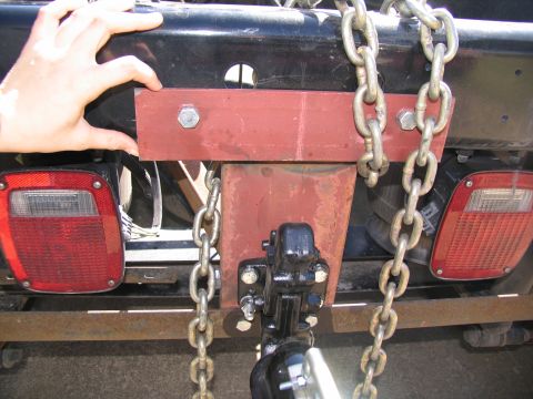 1988 Ford C-350 (Centurion Conversions) - A close-up view of a trailer hitch assembly and safety chains attached to a vehicle's rear bumper.