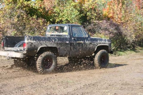 1987 Ford Bronco - A black pickup truck kicks up mud as it drives off-road.