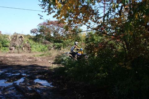 1987 Ford Bronco - A person rides an ATV through a muddy, wooded area on a clear day.