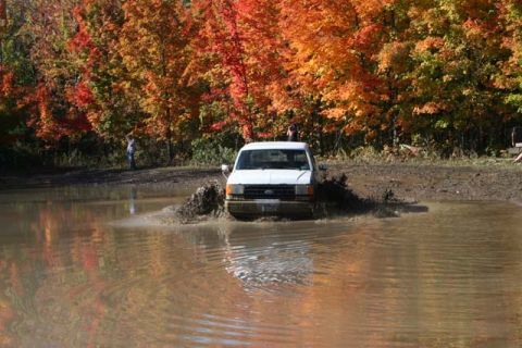 1987 Ford Bronco - A white 1987 Ford Bronco navigates a muddy puddle amidst vibrant autumn trees.