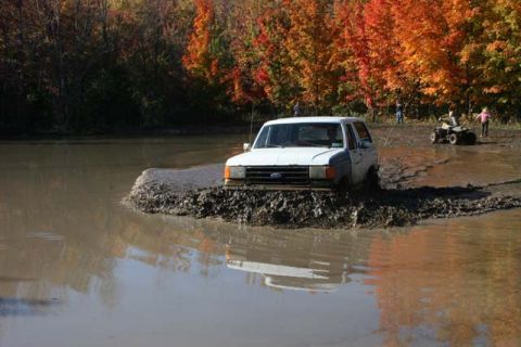 1987 Ford Bronco - A white 1987 Ford Bronco navigates a muddy obstacle course during autumn.