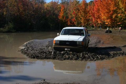 1987 Ford Bronco - White 1987 Ford Bronco navigates a muddy obstacle during an off-road excursion.