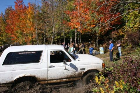 1987 Ford Bronco - A white 1987 Ford Bronco navigates a muddy off-road course during autumn.