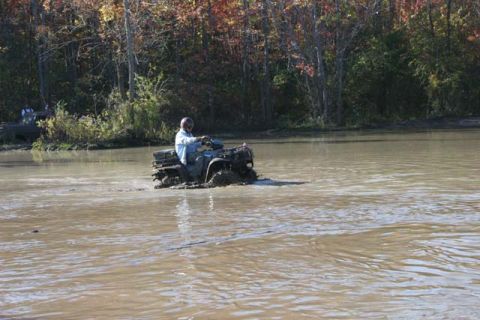 1987 Ford Bronco - An ATV navigates through a muddy body of water, with a second ATV partially visible in the distance.