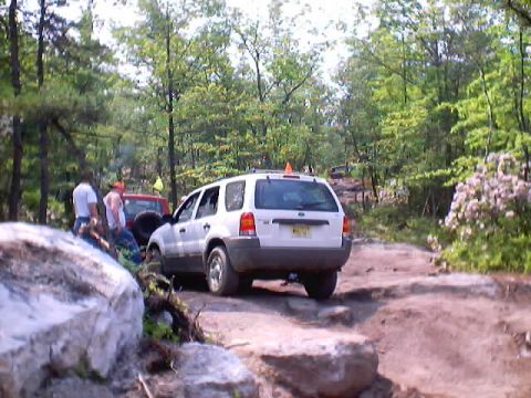 2001 Ford Escape - A white 2001 Ford Escape navigates a challenging off-road course with trees and rocks surrounding the path.