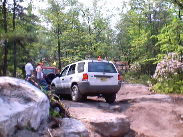 White Ford Escape SUV crawling over rock ledge on a wooded off-road trail