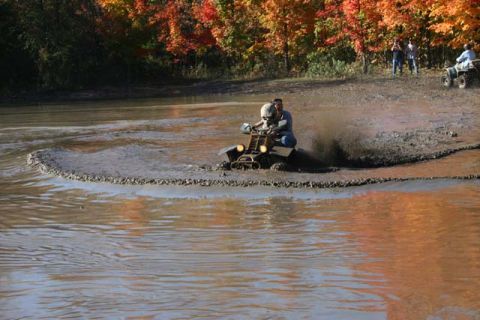 1987 Ford Bronco - People ride ATVs through a muddy area with fall foliage in the background.