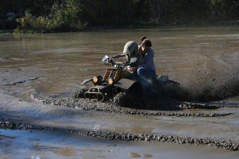 1987 Ford Bronco - An ATV navigates through a muddy water obstacle, creating a significant splash.
