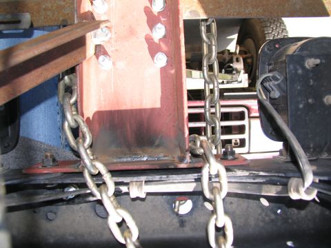 1988 Ford C-350 (Centurion Conversions) - Chains are secured to a red metal beam, with a portion of a vehicle's grille visible in the background.