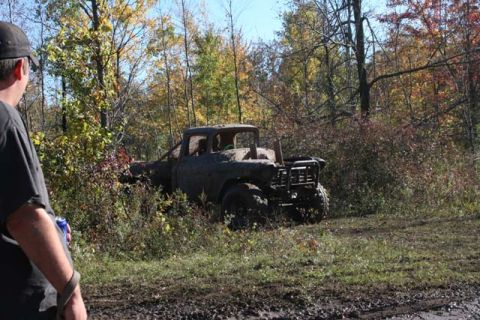 1987 Ford Bronco - Muddy pickup truck sits in a forest clearing surrounded by fall foliage.