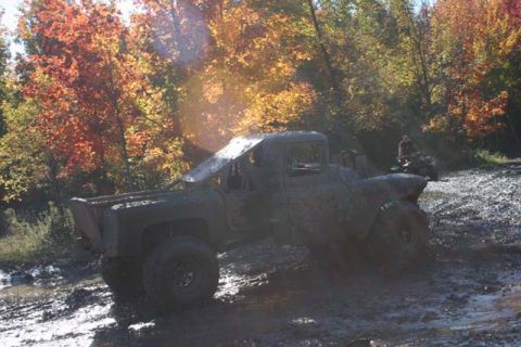 1987 Ford Bronco - A heavily mud-caked pickup truck navigates a challenging off-road course during autumn.