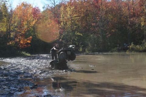 1987 Ford Bronco - An ATV navigates a muddy, watery terrain during autumn, with a second ATV visible in the background.
